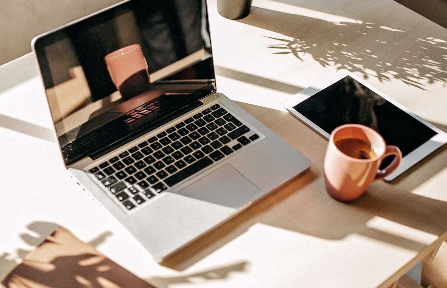 Laptop sitting on a white desk with a coffee cup and ipad